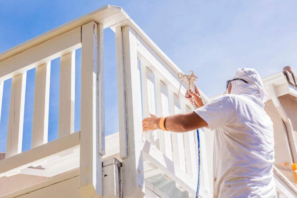 Painter applying white paint to a balcony railing outdoors.