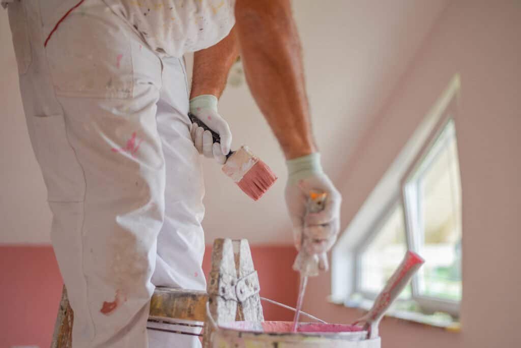 Professional painter applying paint on wall with brush and roller.