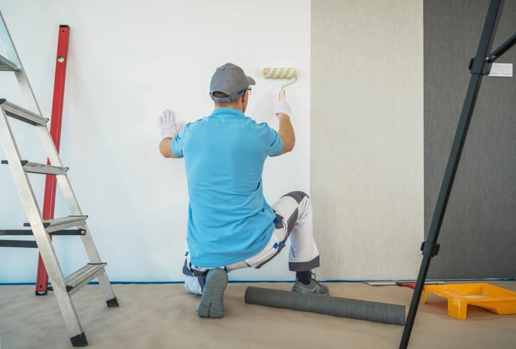 Painter applying wall paint with roller in interior space.