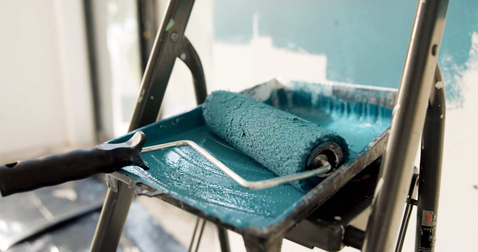 Paint roller and tray with blue paint on a painting cart.