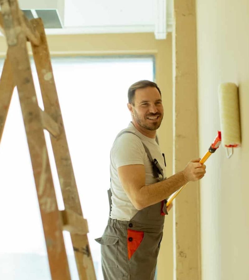Man painting wall with roller in home interior, smiling and working.