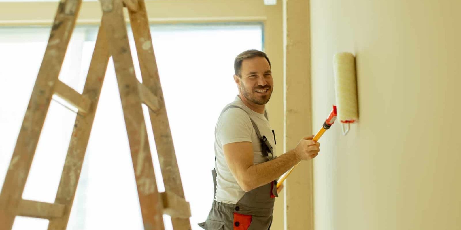 Man painting wall with roller in home interior, smiling and working.